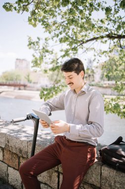 Nehir kenarındaki çitlerde oturan ve tablet arayan mutlu adam.