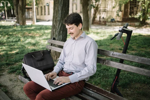 Guy in elegant outfit working on computer in park