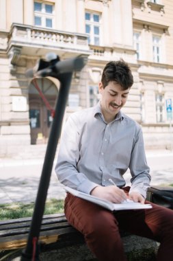 Serbest çalışan adam elektrikli scooterıyla bankta oturuyor.