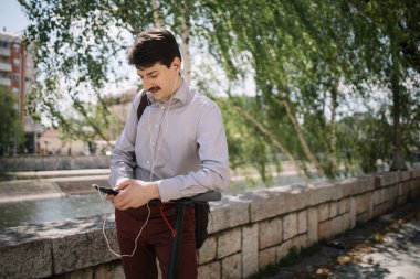 Kulaklıkla dışarıda dururken telefonu kullanan odaklanmış bir adam.