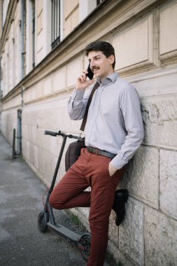 Adam telefonda konuşurken binaya yaslanıyor.