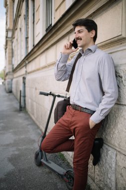 Erkek serbest çalışan, binanın yanında dururken telefonla konuşuyor.