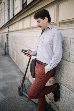 Duvara yaslanan ve akıllı telefon kullanarak e-postalarını kontrol eden adamın profili