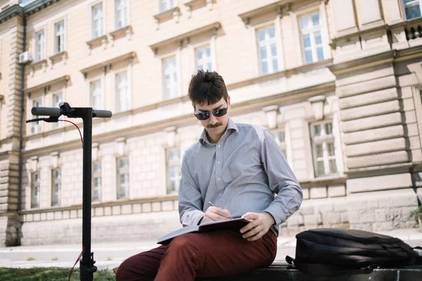 Focused man writing in notebook while sitting on bench outdoor
