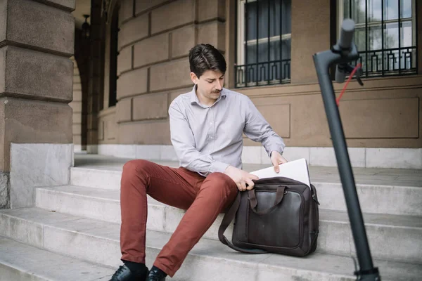 Fiatal férfi húzza laptop táskából, miközben ül a lépcsőn a szabadban — Stock Fotó