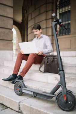 Scooter, laptoplu bulanık bir adamın önünde merdivenlerde oturuyor.