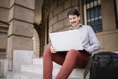 Binanın dışındaki merdivenlerde dizüstü bilgisayarlı gülümseyen adam.