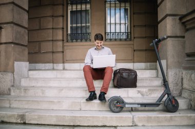 Merdivenlerde otururken dizüstü bilgisayar kullanan mutlu bir adam.