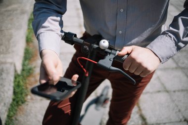 Siyah akıllı telefon kullanarak elektrikli scooter kullanan kırpılmış bir adam.