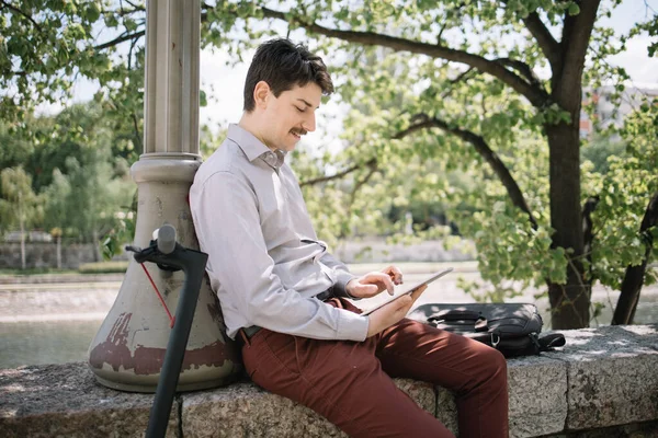 Profile of man working on tablet while sitting with electric scooter outdoor