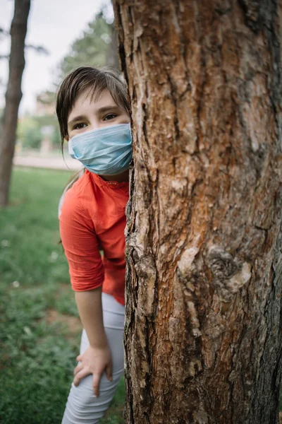 Happy child wearing antivirus mask while standing behind tree
