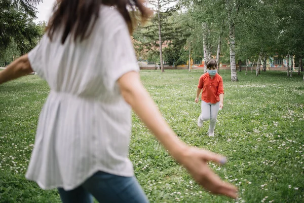 Moeder klaar om haar kind te knuffelen met medisch masker in park — Stockfoto