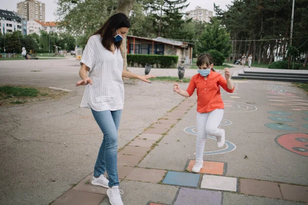 Slim lady and girl with face masks playing in the park during COVID-19 outbreak