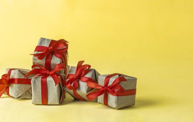 El işi kağıdına sarılı hediye kutuları ve sarı arka planda kırmızı saten kurdele. Bahar, bir kadın için bir hediye, tatil havasından bir hediye. Yeni yıl Noel dekoru. Popüler eğilim