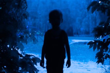 Mavi gece ışığında, ağaçların arasındaki koridorda bir çocuğun silueti. Macera konsepti, mistisizm ve uyurgezerlik.