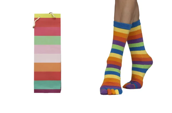 Las piernas femeninas en calcetines de puntillas de colores van a una bolsa de regalo a rayas de color — Foto de Stock