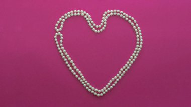 Pembe arka planda kalp şeklinde inci boncuklar.