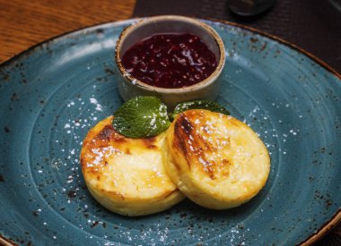 Geleneksel çocuk kahvaltısı ve peynirli kekler, süzme peynirli krepler, şuruplu ve reçelli bir tabakta. Yaratıcı hizmet, kafede kahvaltı. Sağlıklı ve lezzetli yemekler..