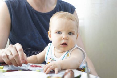 Küçük bebek masada babasının kucağına oturur ve yemek beklerken başını çevirir. Restoran kafeteryası, kapalı mutfak..