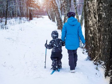 4-6 years boy rides and walks on skiing with young mother. First steps in sport active lifestyle of child. Care and support parents. No faces people with their backs. Winter family outdoor activities