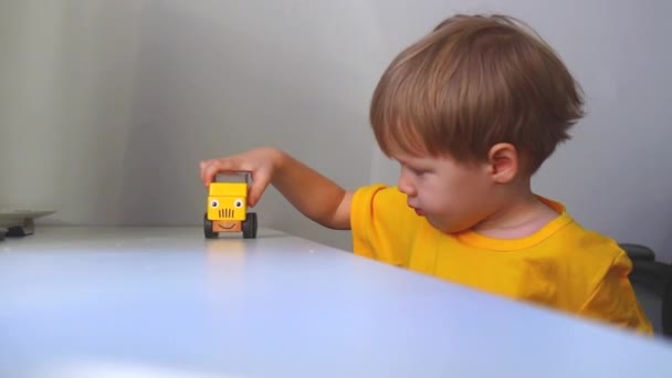Junge rollt ein gelbes Auto mit aufgemaltem Gesicht auf einen weißen Tisch — Stockvideo