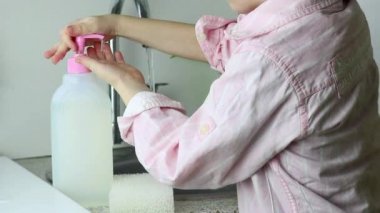 Çocuk çocuk, renksiz bebek jeliyle bir şeker kutusuna tıklıyor ve ellerini musluğun altında suyla yıkıyor. Çocuk zararsız bir ürünle ellerini sabunluyor. Çevre dostu mutfak konsepti