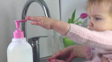 Annelerin kadın elleri, bebeğin ellerini çocuklar için güvenli bir aletle yıkamasına yardım eder. Çocuklar için renksiz çevre dostu jel sabunu