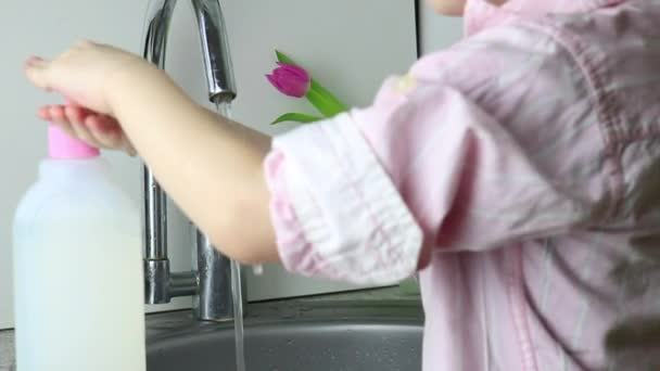 Хлопчик-дитина натискає на диспенсер з безбарвним гелем для миття дитини і миє руки під краном з водою. Малюк миє руки небезпечним продуктом. Концепція екологічно чистої кухні — стокове відео