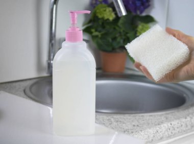 El yıkama ve bulaşık yıkama için şeffaf jel benzeri ürün. Biyolojik çözünebilir plastik ve çevre dostu. Lavabo ve su musluğunun arkasında beyaz bir mutfak var.