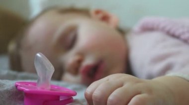 Uyuyan bir bebeğin portresi. Yürüyen çocuk emzik olmadan uyuyor. Emzik ağzından düşmüş ve yakınlarda bir yerde duruyor. Dönüşümlü olarak emziğe ve bebek yüzüne odaklan. Yan görünümü kapat