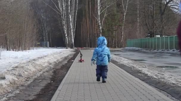 Niño corriendo montando un scooter en la acera con la espalda a la cámara en un scooter rojo — Vídeos de Stock