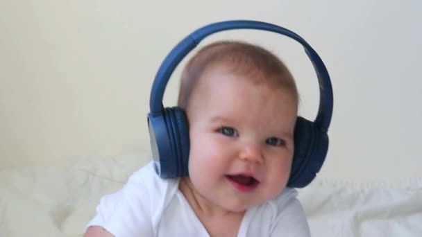 Criança bebê Criança feliz sorrindo em fones de ouvido azuis sem fio em um fundo branco. O conceito de tecnologia aprendendo desde o nascimento e música fina — Vídeo de Stock
