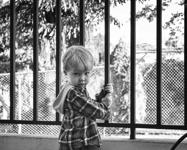 Małe europejskie dziecko stoi obok kratownicy w kwarantannie smutne. Zamknięte przedszkole i podróże. Izolacja koronawirusów, samoizolacja — Zdjęcie stockowe