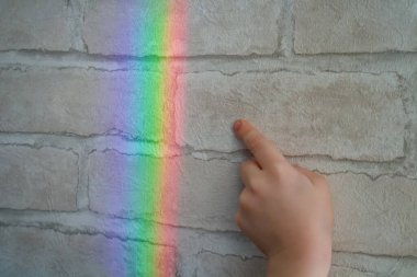 Tuğla duvar kağıdından yapılmış gerçek bir gökkuşağı. Çocuğun eli gökkuşağının yansımasına dokunmak istiyor..