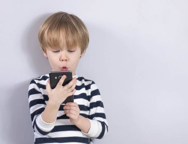 Cep telefonunu elinde tutan sevimli çocuğun yakın plan portresi. Gri arka planda gördükleri karşısında şok oldu..