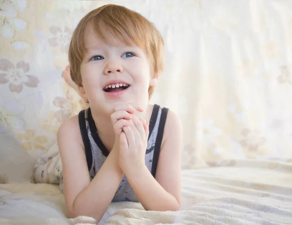 Klein blond kind jongen ligt op een bank op zijn buik en dromen kijken omhoog met een glimlach — Stockfoto
