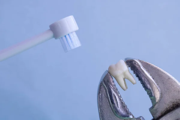 Электрическая зубная щетка будет чистить рваный зуб зажимается большими плоскогубцами на синем медицинском фоне. Копирование пространства — стоковое фото
