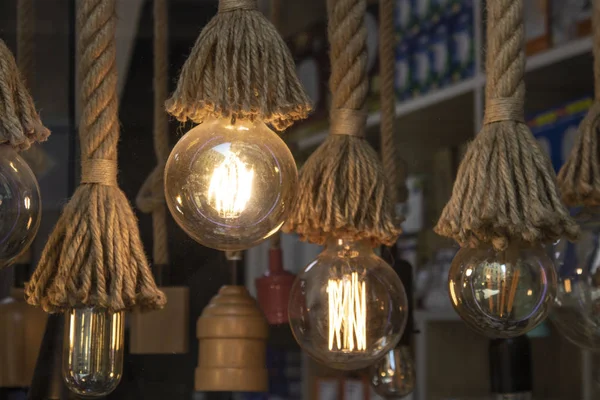 Five round retro lamps with warm light are hung on a decorative rope cable on a brown warm background.