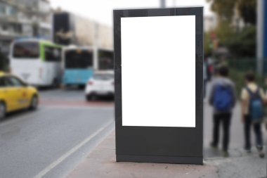 Yol kenarındaki boş beyaz dikdörtgen reklam panosu. Soldan iki genç geliyor..