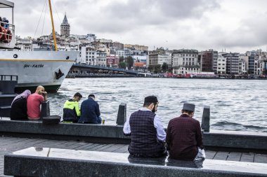 Bereli iki adam deniz kenarında sohbet ediyor. Eminonu plajı ve oradaki insanlar denizi izliyor..