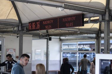 Kadıköy feribot iskelesi. Eminonu kıyısından, yolcular feribota binmek için gelirler. Öndeki işaretin üstünde saatler ve kadikoy var..