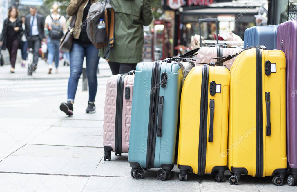 Close up of suitcases for sale on the pavement. Different colors and sizes. People walking in front of the pavement.