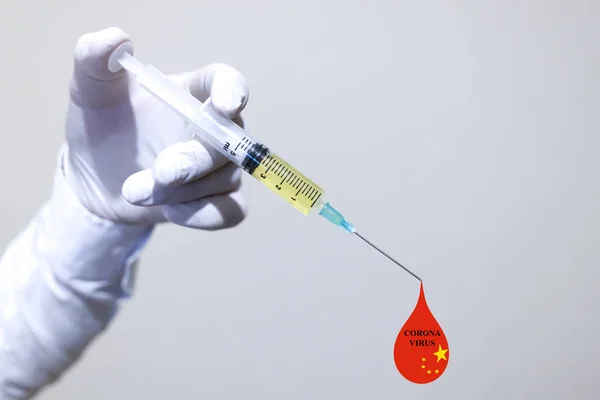 En hand med handskar i vit färg. Vaccinet hålls i handen. Droppar i rött på nålspetsen. Kinesisk flagg. — Stockfoto