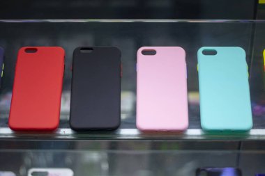 Dükkan vitrininde üç farklı renk telefon kılıfı var. Önünde bir bardak var..
