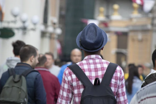 Un adolescente con una camisa a cuadros, un sombrero y una mochila. El hombre se da la vuelta y es fotografiado afuera . — Foto de Stock