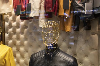 Bir giyim mağazasının önünde. Metalik cansız mankenler mağazanın arka planında çeşitli malzemelerle duruyorlar..