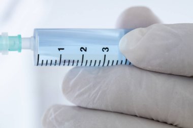 Doktor eldiveninde mavi sıvı olan şırıngayı tutuyor. Şırınga odaklandı.
