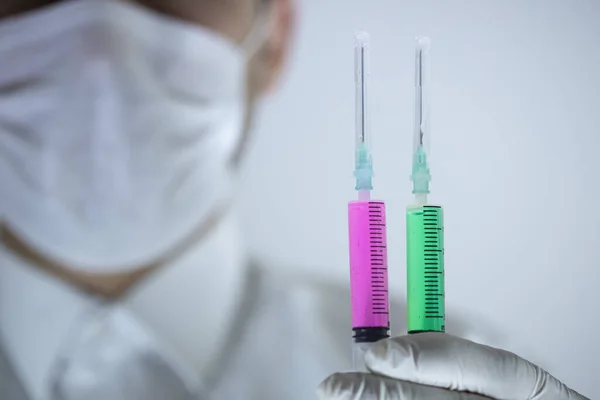El médico con una máscara en la boca tiene dos vacunas en la mano. Vacunas en colores rojo y verde. Estudio de rodaje. De cerca. . —  Fotos de Stock
