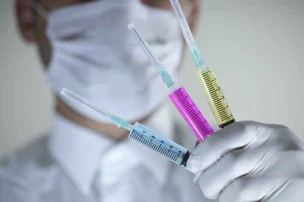 El médico con una máscara en la boca tiene dos vacunas en la mano. Vacunas en colores rojo y verde. Estudio de rodaje. De cerca. . —  Fotos de Stock