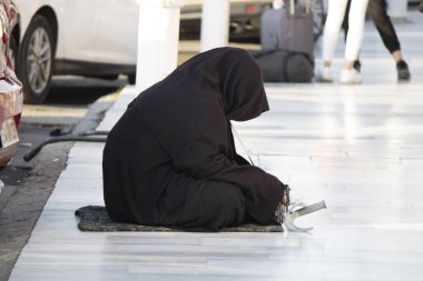 Siyah burka giymiş bir kadın mermer parke üzerinde yalvarıyor. Suriyeli göçmen.
